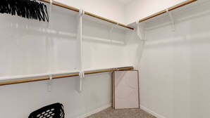 Un dressing avec des tringles en bois, un panier en plastique noir et un mur blanc.