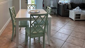 Ein Essbereich mit einem weißen Tisch und grünen Stühlen, einem Deckenventilator und Blick ins Freie durch eine Tür.