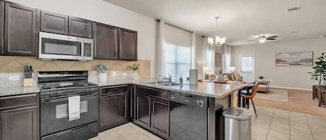 A modern kitchen with dark cabinetry, stainless steel appliances, and a tiled floor.