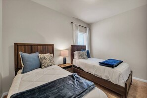 Un dormitorio con dos camas, una mesita de noche con lámpara y una ventana con cortinas.