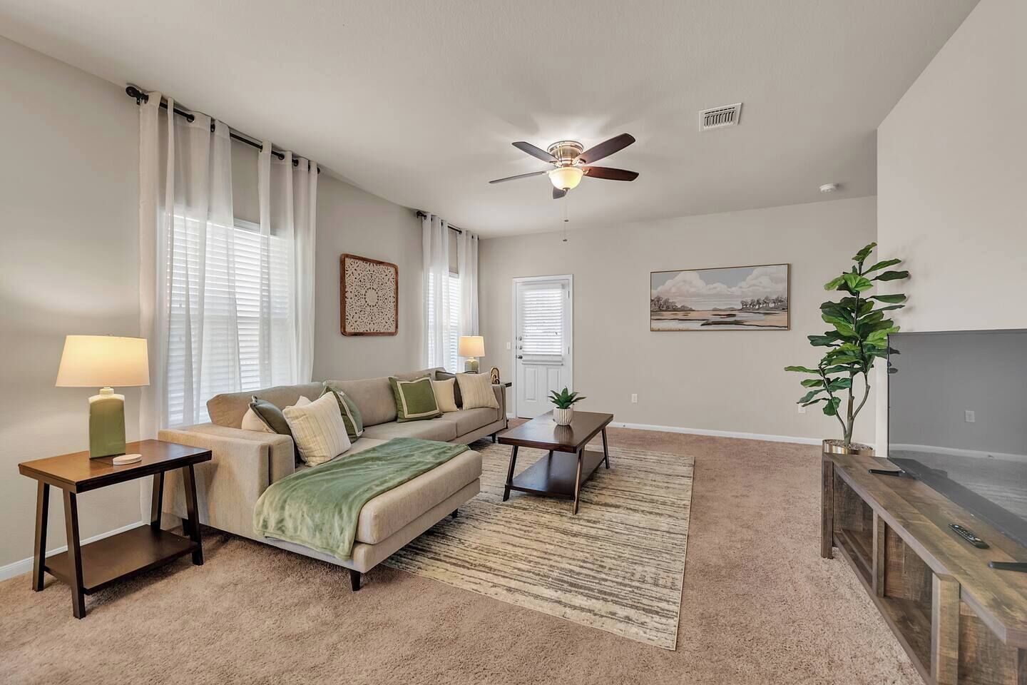 A living room with a sofa, two side tables, a coffee table, a ceiling fan, a painting, and a TV stand.