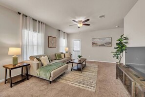 A living room with a sofa, two side tables, a coffee table, a ceiling fan, a painting, and a TV stand. - Cedar Park Executive Retreat (Cedar Park)