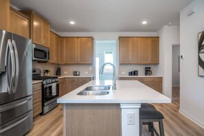 A modern kitchen with wooden cabinets, stainless steel appliances, a central island, and a view to the dining area.