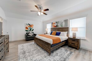 Une chambre à coucher avec un lit en bois, un ventilateur de plafond, une table de chevet avec une lampe, une chaise et des œuvres d’art accrochées aux murs.