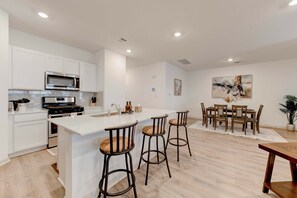 Une cuisine moderne avec des meubles blancs, une cuisinière en acier inoxydable et un four à micro-ondes. On y trouve également un coin repas avec une table et des chaises en bois.