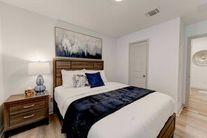 A bedroom with a bed, a nightstand, a lamp, a painting, and a door.