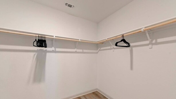 A room with white walls, a wooden floor, and a built-in closet with wooden shelves and black hangers. - 4BR Corporate Stay in Hutto (Hutto)