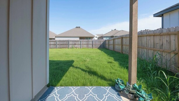 A backyard with a wooden fence, a grassy lawn, and a house in the background.
