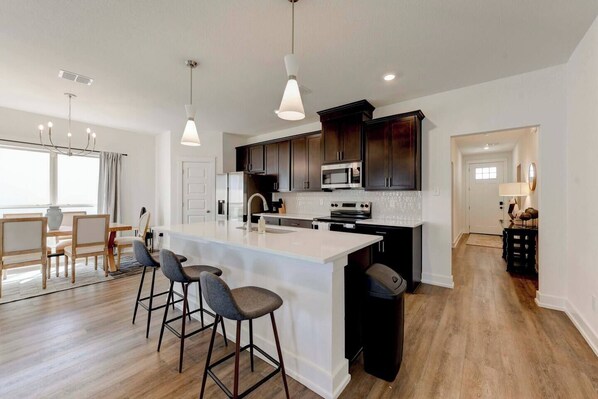 A modern kitchen with a central island, bar stools, dark wood cabinets, and stainless steel appliances.