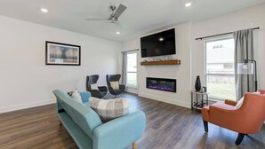 A modern living room with a sofa, two armchairs, a fireplace, a TV, and a ceiling fan.