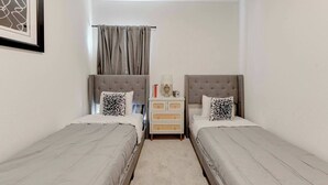 A bedroom with two beds, a nightstand, a framed picture, and a window with curtains.