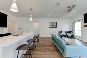 Una cocina moderna con una isla blanca, taburetes de bar, un sofá y un ventilador de techo.