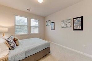 A bedroom with a bed, two windows, and wall art.