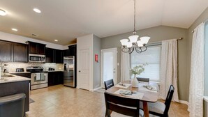 A modern kitchen with dark cabinets, stainless steel appliances, and a dining area with a wooden table and chairs. - North Austin Corporate-Ready 3BR (Austin)