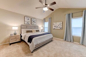 A bedroom with a bed, nightstands, a ceiling fan, and artwork on the walls.