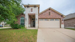 A two-story house with a stone entrance, a garage, and a well-maintained lawn. - North Austin Corporate-Ready 3BR (Austin)