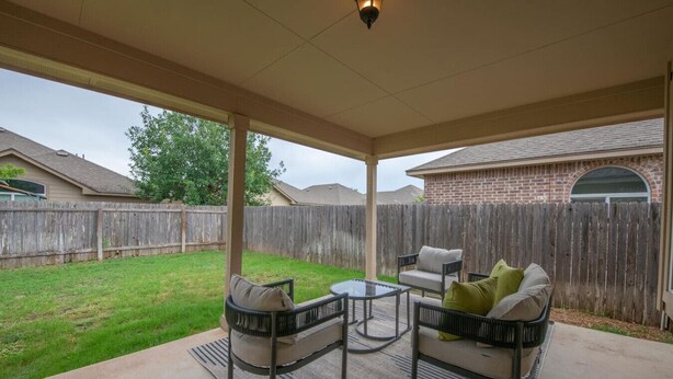 A covered patio with outdoor furniture, a brick building in the background, and a wooden fence. - North Austin Corporate-Ready 3BR (Austin)