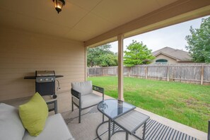 A covered patio with a grill, a glass table, and a sofa with cushions.