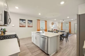 A modern kitchen with a central island, dining area with chairs, and a living space with a sofa and lamp.