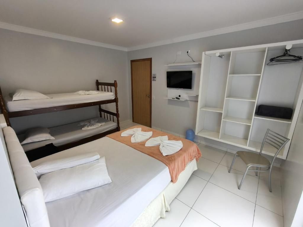 A room with a bunk bed, a desk with a chair, a television, and a wardrobe with shelves.