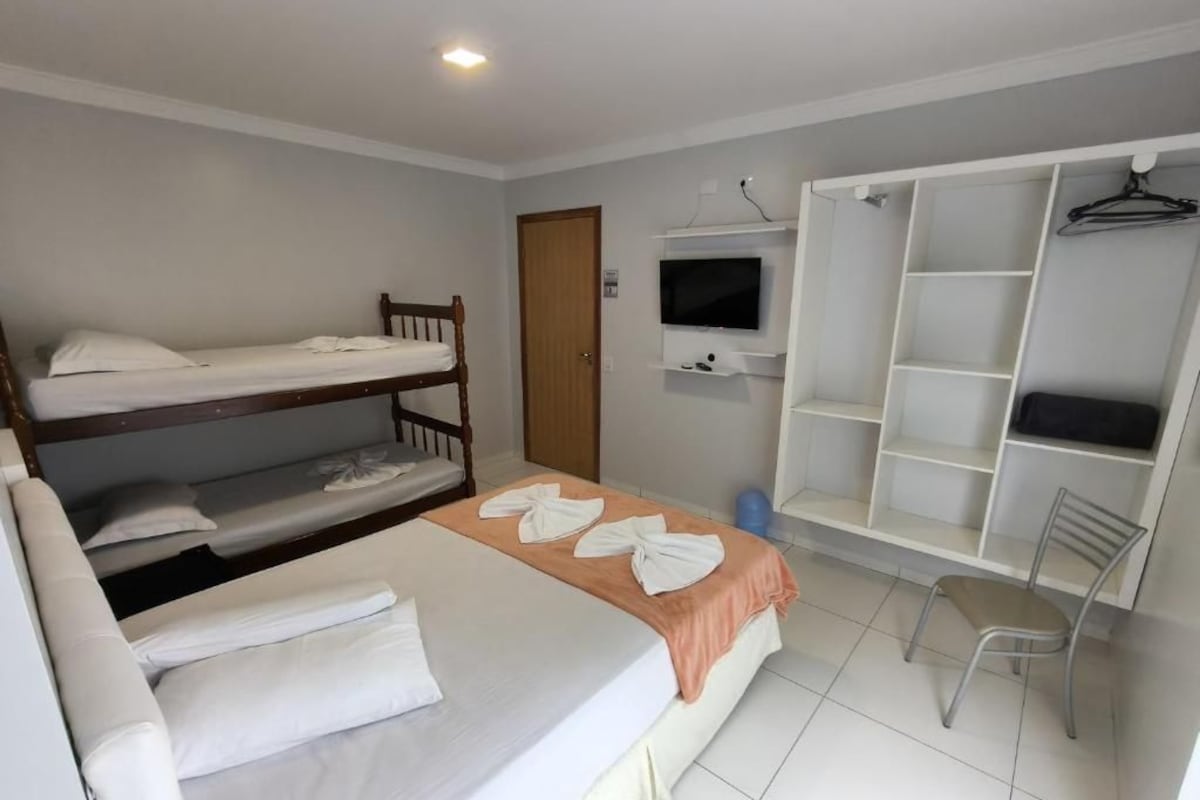 A room with a bunk bed, a desk with a chair, a television, and a wardrobe with shelves.