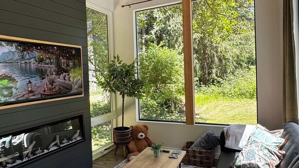 Un salon moderne doté d’une cheminée, de grandes fenêtres et offrant une vue sur la verdure.