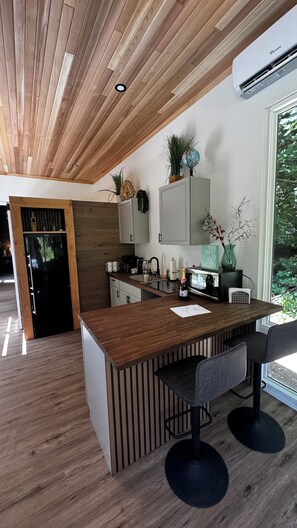 Een moderne keuken met een houten plafond, een geïntegreerd kookeiland met barstoelen en uitzicht op groen.