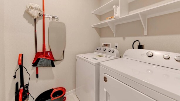 A laundry room with a washing machine, a dryer, a broom, and a mop.
