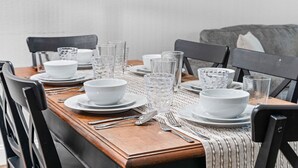 A dining table set with white plates, bowls, and clear glasses, surrounded by black chairs. - Peaceful Golf Course View + Pool + Sunroom (Branson)