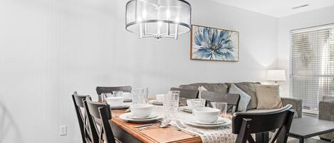 A dining area with a wooden table set for four, a modern chandelier, and a large abstract painting on the wall.