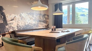 Comedor con mesa de madera, dos lámparas colgantes y un mural de montañas en la pared.