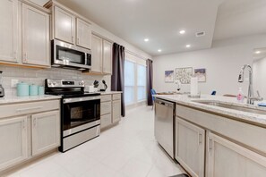 A modern kitchen with stainless steel appliances, light-colored cabinetry, and a large island with a sink. - Luxurious 4-Bedroom House (Temple)