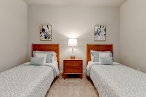 Une chambre avec deux lits simples, une table de chevet avec une lampe et deux tableaux accrochés au mur.