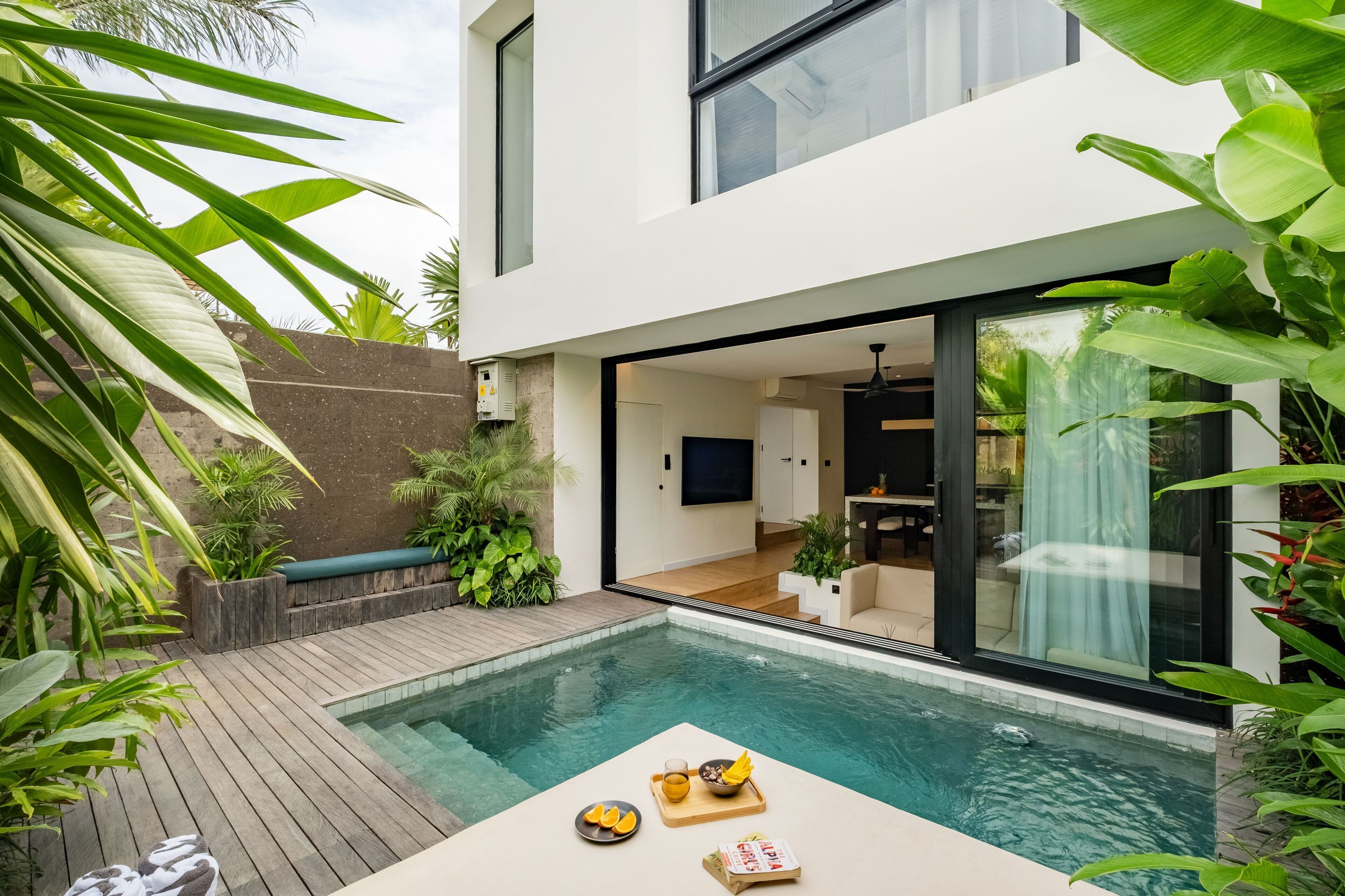A modern house with a swimming pool, wooden deck, and lush greenery.