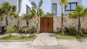 A modern building with a stone wall, a wooden gate, and palm trees. - Club Suma Villa Bingin (Pecatu)