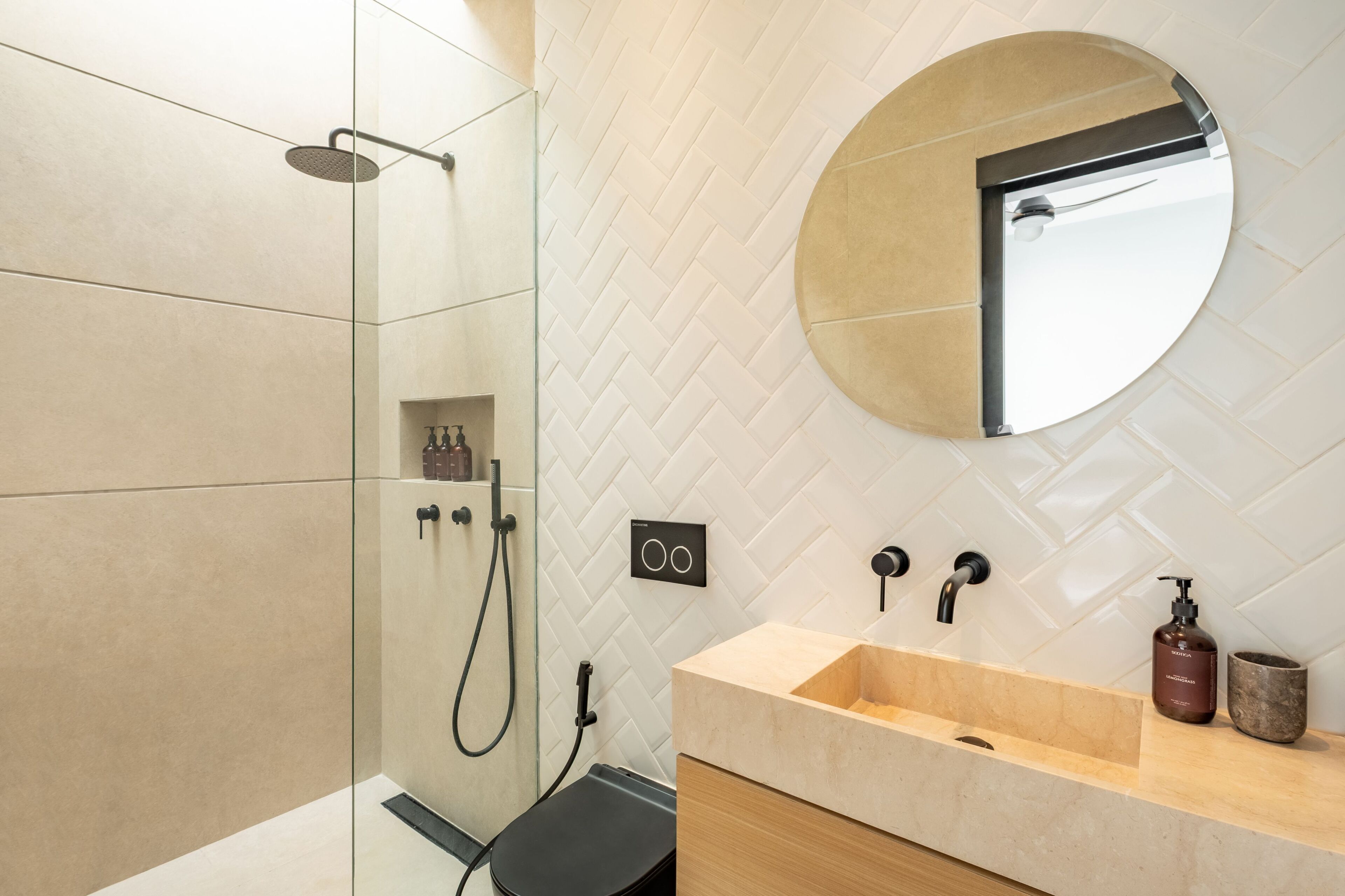 Een moderne badkamer met een douchecabine van glas, een beige wastafel met een houten aanrechtblad en een ronde spiegel boven de wastafel.