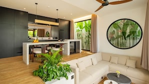 A modern living room with a sofa, a coffee table, and a kitchen area with a dining table. - Club Suma Villa Bingin (Pecatu)