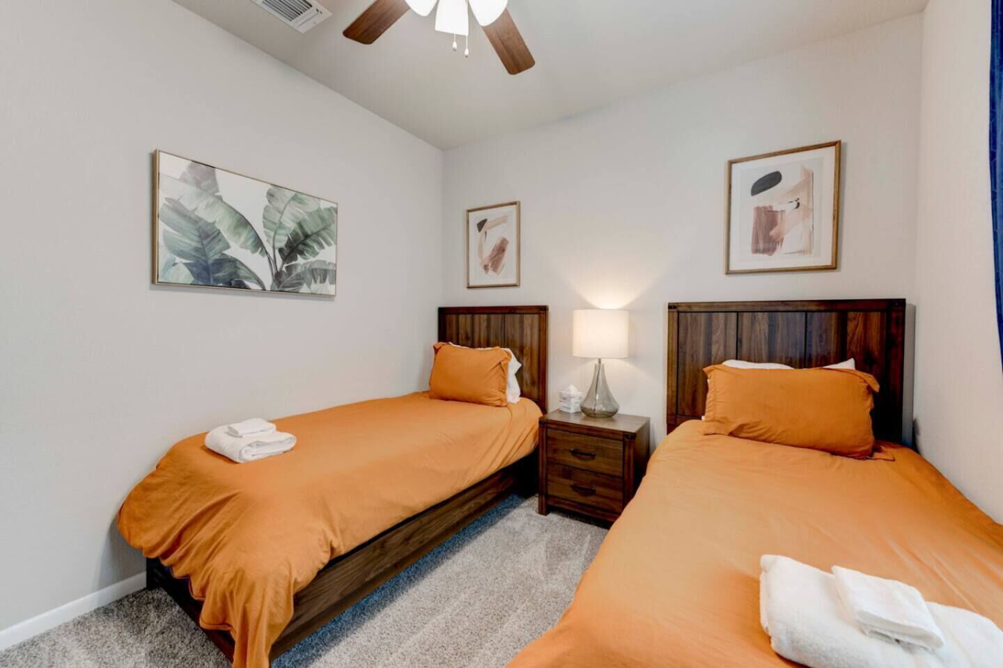 A hotel room with two beds, a nightstand with a lamp, and artwork on the walls.