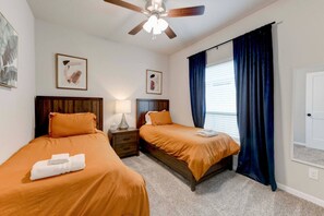 A hotel room with two beds, a ceiling fan, a nightstand with a lamp, and a window with curtains. - Manor Gateaway in Manor (Manor)
