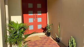 A red door with glass panels, potted plants, and a tiled entrance area.