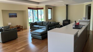 A modern living room with a sectional sofa, a dining area with a kitchen island, and a large window offering a view of the outdoors.