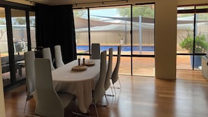 A dining area with a table set for six, large windows, and a view of a backyard with a pool.