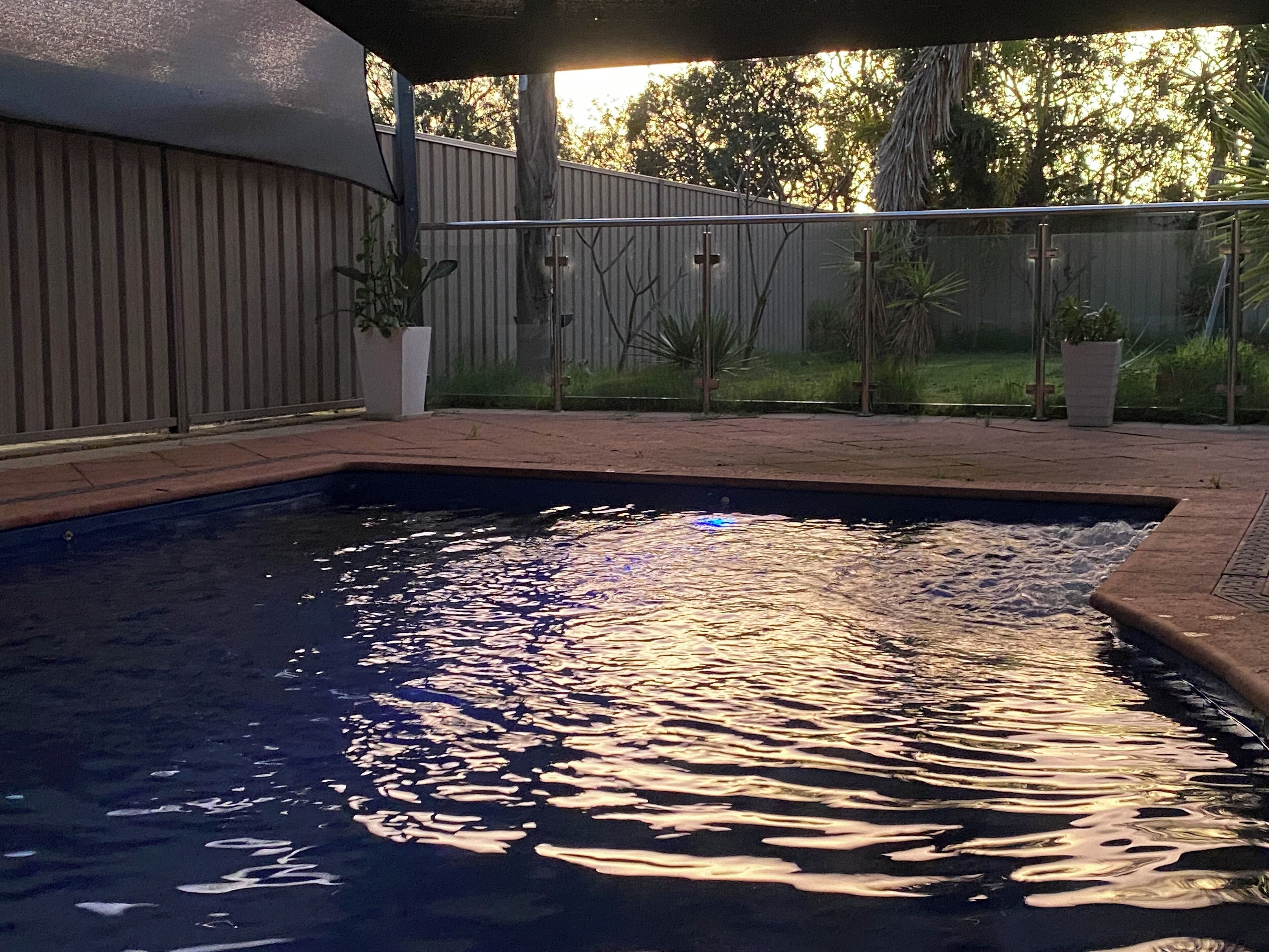 A swimming pool with a wooden deck and a metal fence.
