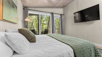 A bedroom with a bed, a chair, a TV, and a window with a view of trees.
