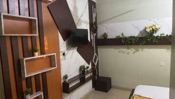 A modern bathroom with a marble wall, wooden shelving, a flat-screen TV, and a small potted plant.