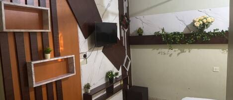 A modern bathroom with a marble wall, wooden shelving, a flat-screen TV, and a small potted plant.