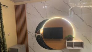 A modern living room with a TV mounted on a curved wall, a small shelf with a plant, and a decorative light fixture.