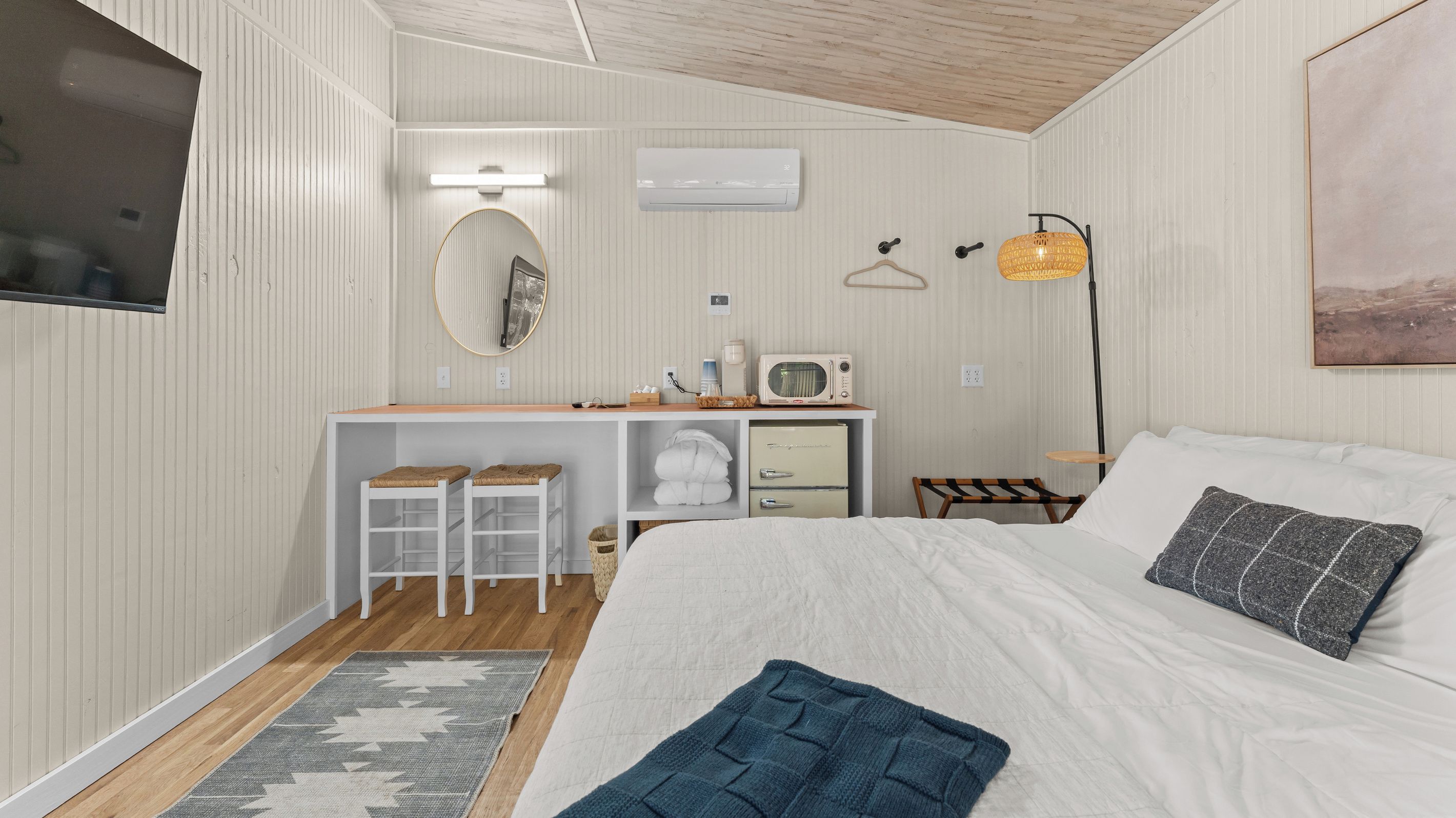 Un dormitorio con cama, escritorio con silla, microondas y lámpara colgante.