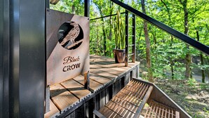 Une terrasse en bois avec une rambarde en métal, une enseigne indiquant « Black Crow », et un pot de fleurs.