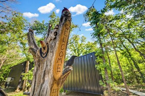 Een houten paal met 'WELCOME' erin gekerfd, omringd door bomen en een metalen constructie op de achtergrond.